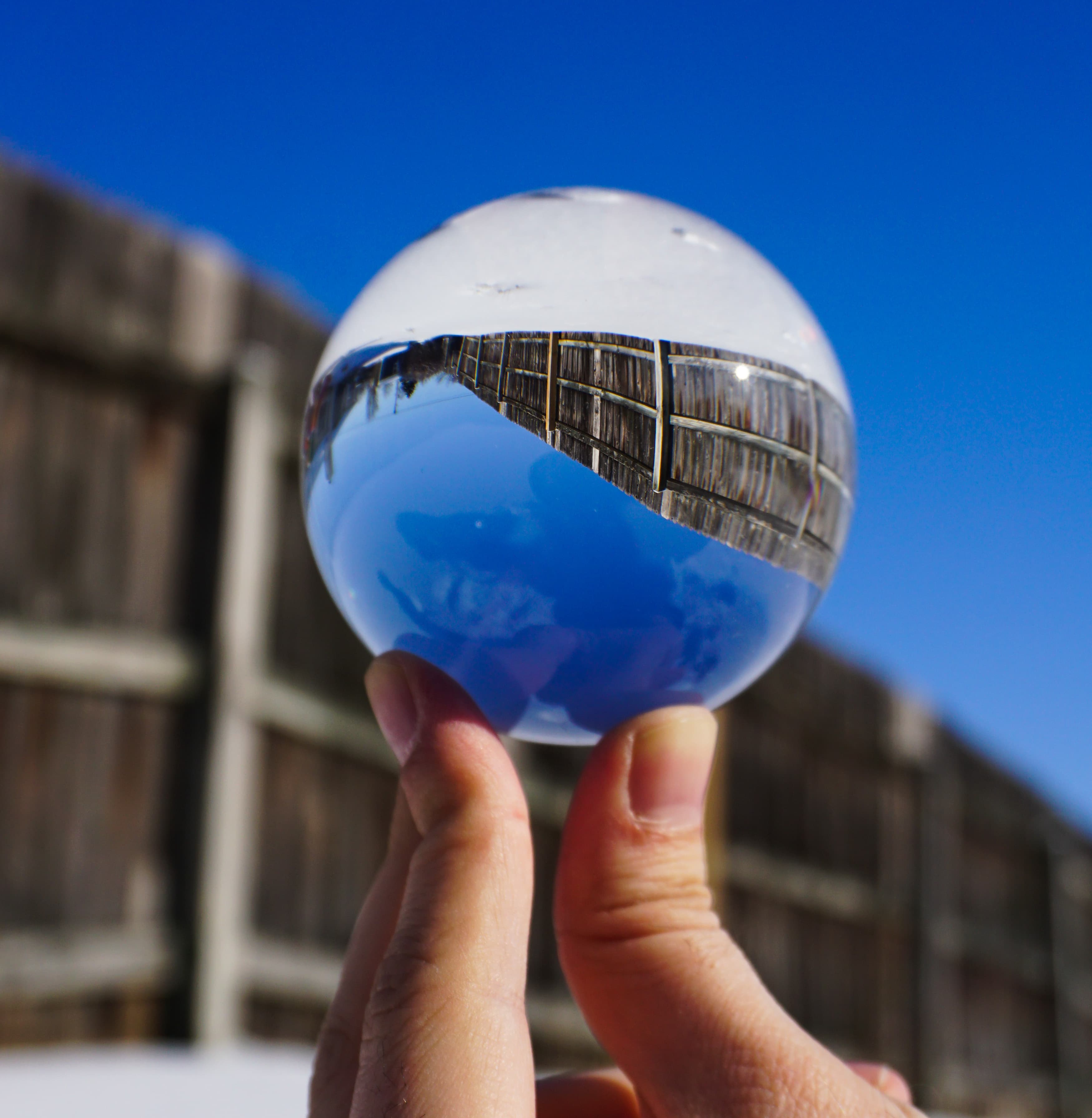 Lensball held in bright winter sunlight with blue sky and fence reflected inside